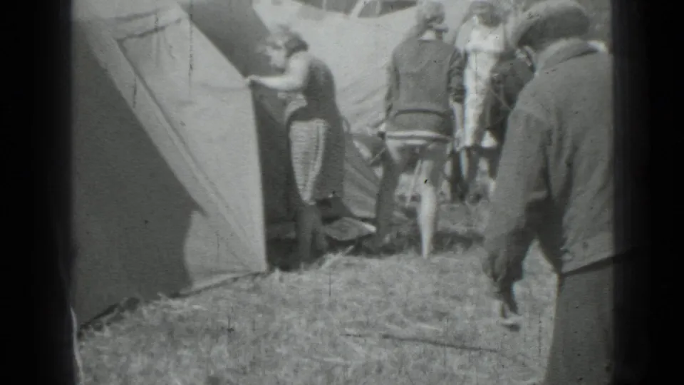 1967 Saint Petersburg home-movie frame showing adults near canvas tents as a dog enters the grassy foreground.