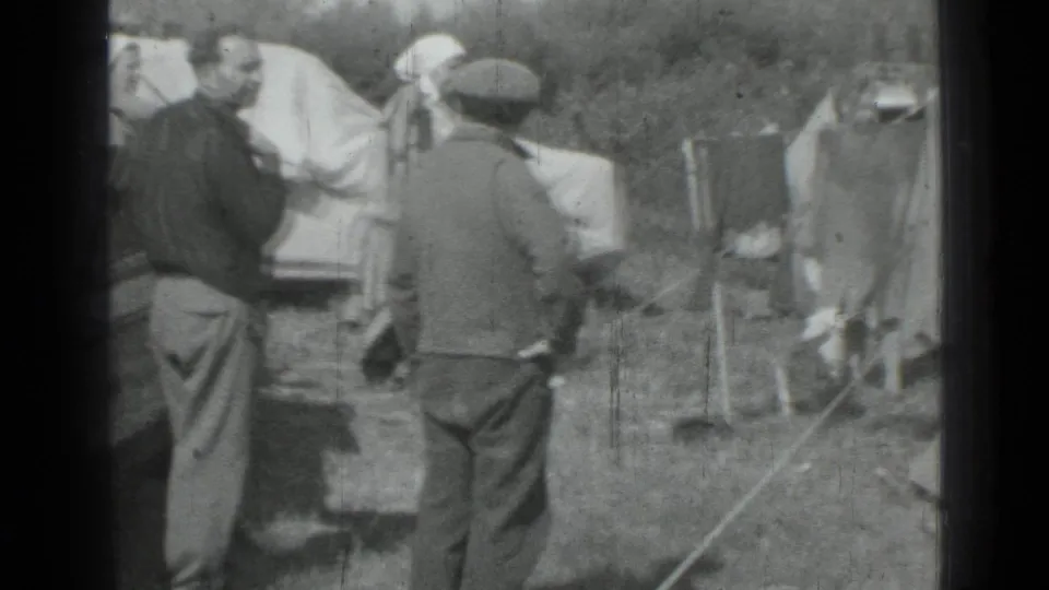 1967 Saint Petersburg home-movie frame showing adults at a grassy campsite with tents, camp poles, and laundry on a line.