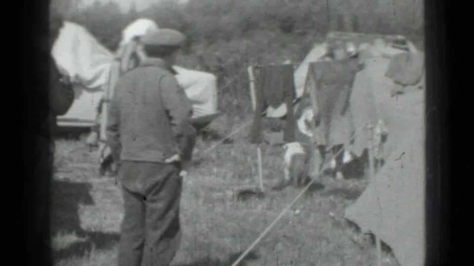 1967 Saint Petersburg camping frame with an adult in a cap, canvas tents, clothesline, and outdoor gear in black-and-white 8mm.