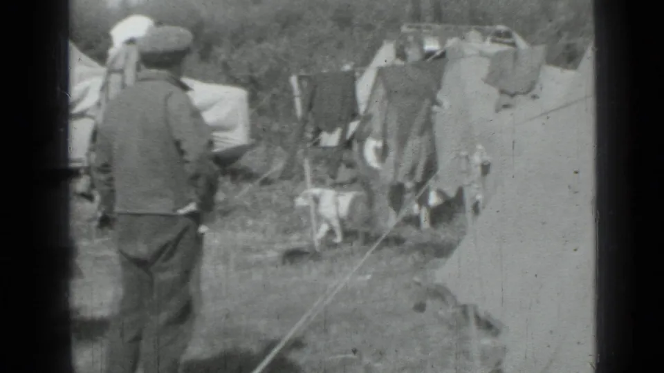 1967 home-movie frame from Saint Petersburg showing adults near tents, hanging laundry, and campsite gear on grass.