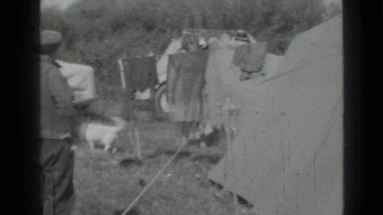 A small white dog crosses the campsite as adults stand near tents and laundry in 1967 Saint Petersburg footage.