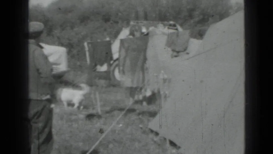 A small white dog crosses the campsite as adults stand near tents and laundry in 1967 Saint Petersburg footage.