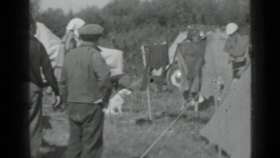 Adults in coats and caps move around a Saint Petersburg campsite with tents, hanging laundry, and a small dog nearby.
