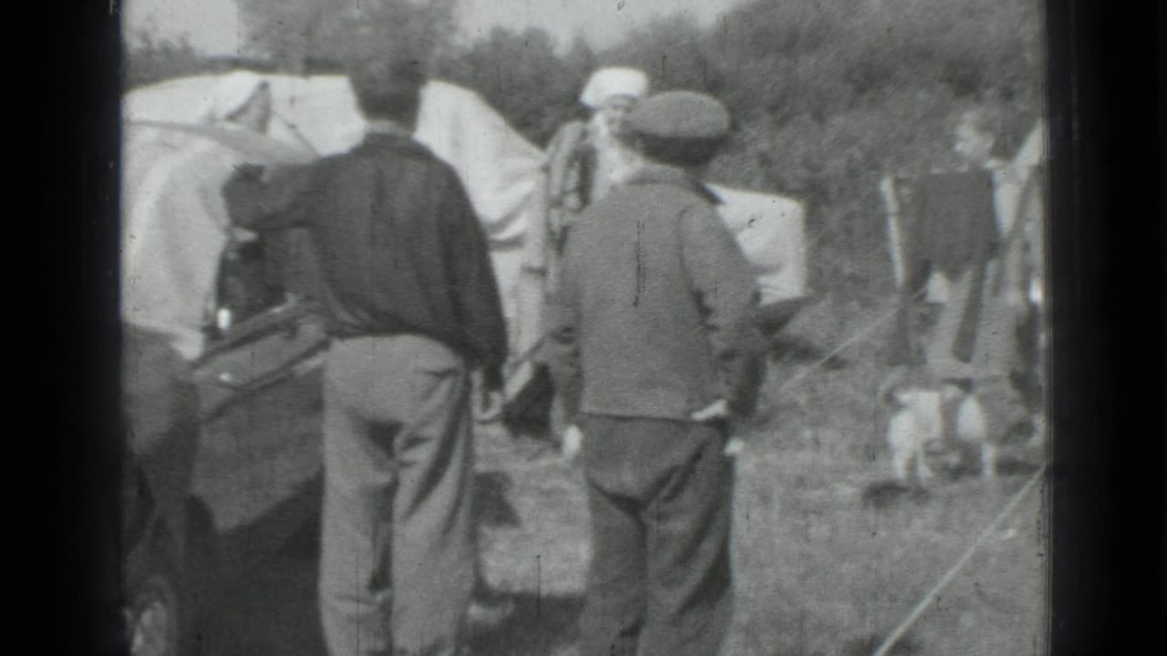 1967 Russia home-movie frame showing men near a parked car with blankets drying in a grassy roadside setting.