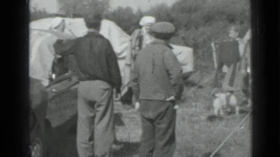 1967 Russia home-movie frame showing men near a parked car with blankets drying in a grassy roadside setting.