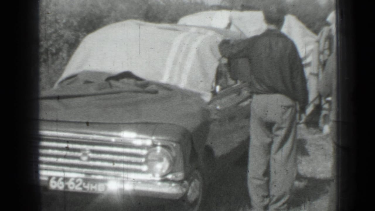 Man beside the front of a parked car with blankets over the roof.