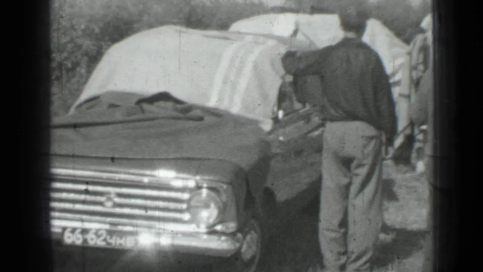 A man stands beside a parked sedan with blankets draped above it in the 1967 Russia roadside scene.