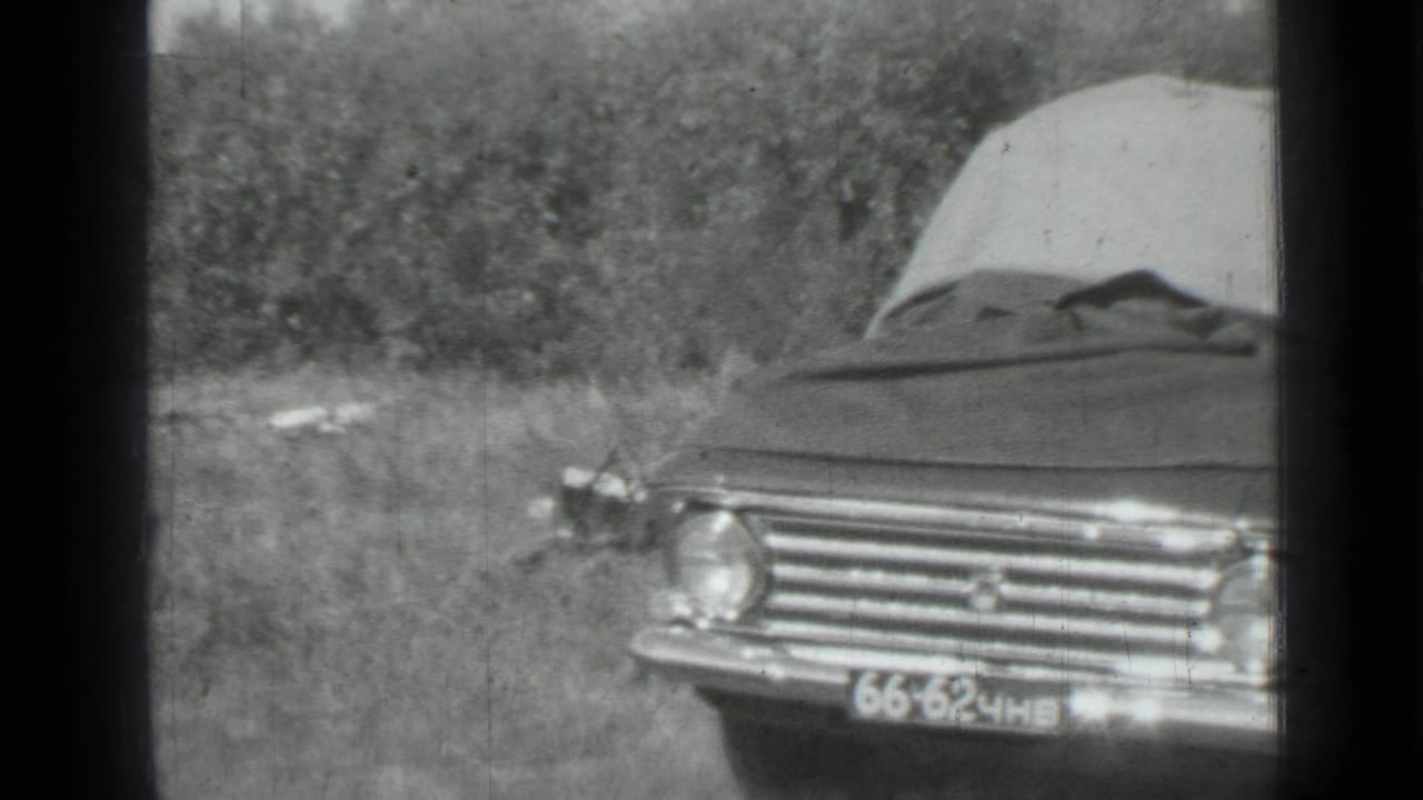 1967 Saint Petersburg frame showing a tarp-covered sedan parked in a grassy field with trees behind it.