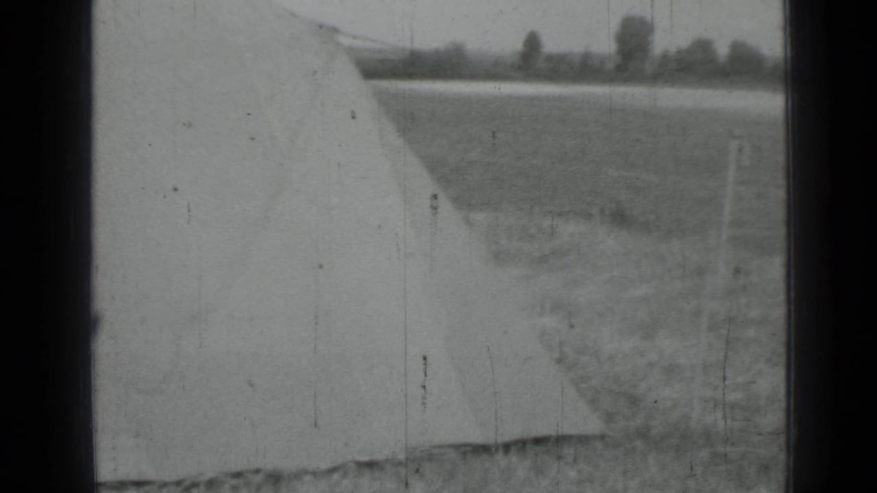 Black-and-white 1967 home-movie frame near Saint Petersburg showing a large pale tarp or fabric edge in an open rural field.
