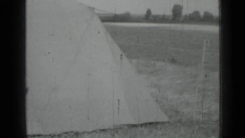 Black-and-white 1967 home-movie frame near Saint Petersburg showing a large pale tarp or fabric edge in an open rural field.