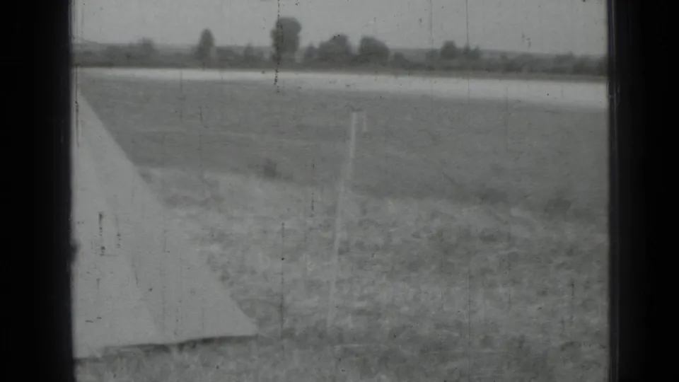 Monochrome 8mm frame showing a rural field, pale tarp edge, posts, and a distant tree line in the reported Saint Petersburg area.