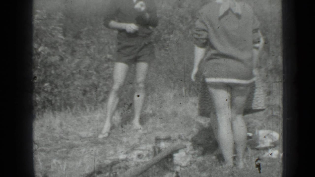 Two women in dresses stand outdoors near a small pan on the ground.