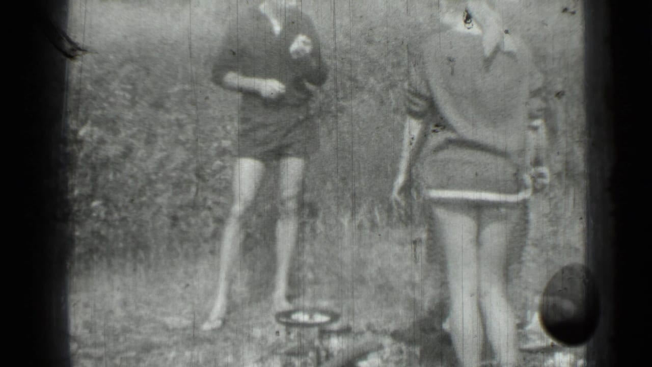 Saint Petersburg home-movie frame from 1967 with two women outdoors near a small pan, framed by heavy film edges.