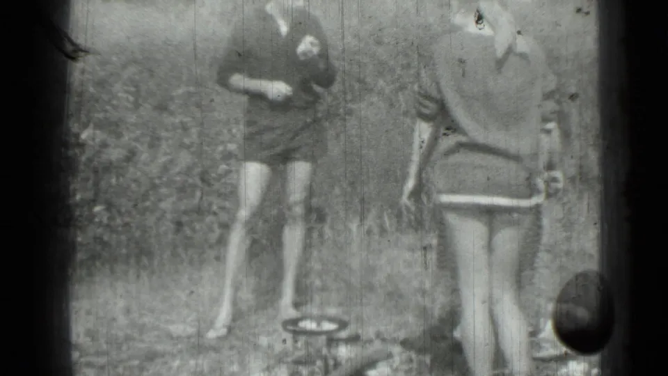 Saint Petersburg home-movie frame from 1967 with two women outdoors near a small pan, framed by heavy film edges.