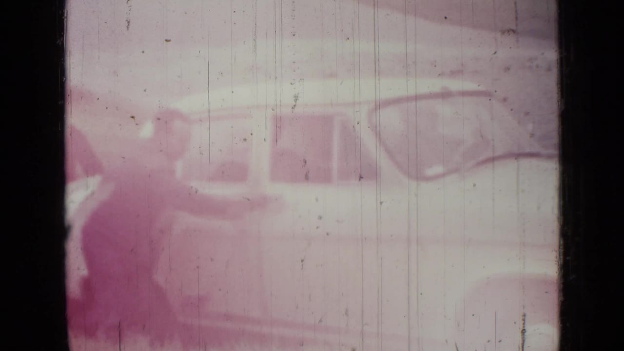 Faded 1967 Saint Petersburg 8mm frame showing a pale sedan on a roadside, softened by purple color shift and film wear.