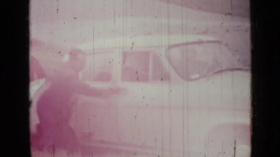 Faded 1967 Saint Petersburg 8mm frame showing a pale sedan on a roadside, softened by purple color shift and film wear.