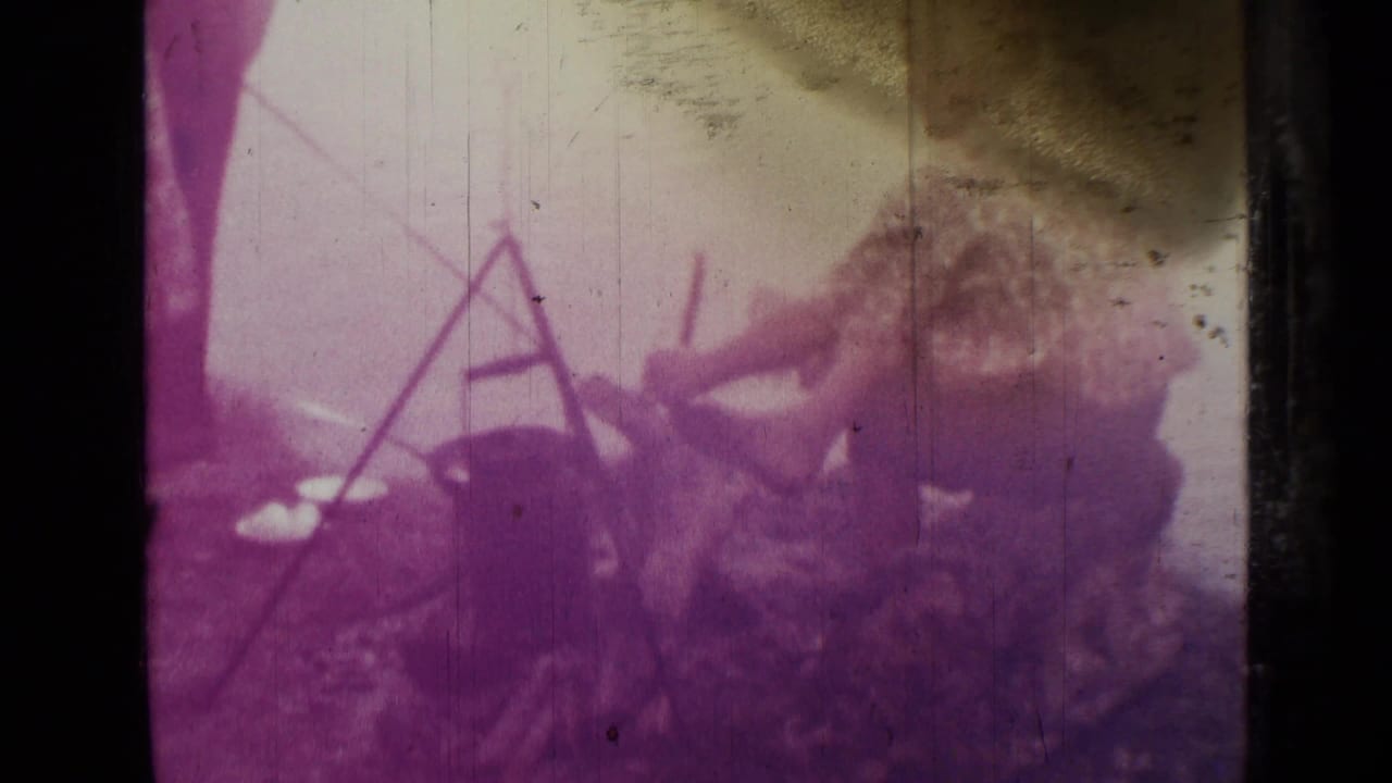 1967 Saint Petersburg home-movie frame with people gathered near a tripod cooking setup over open ground.