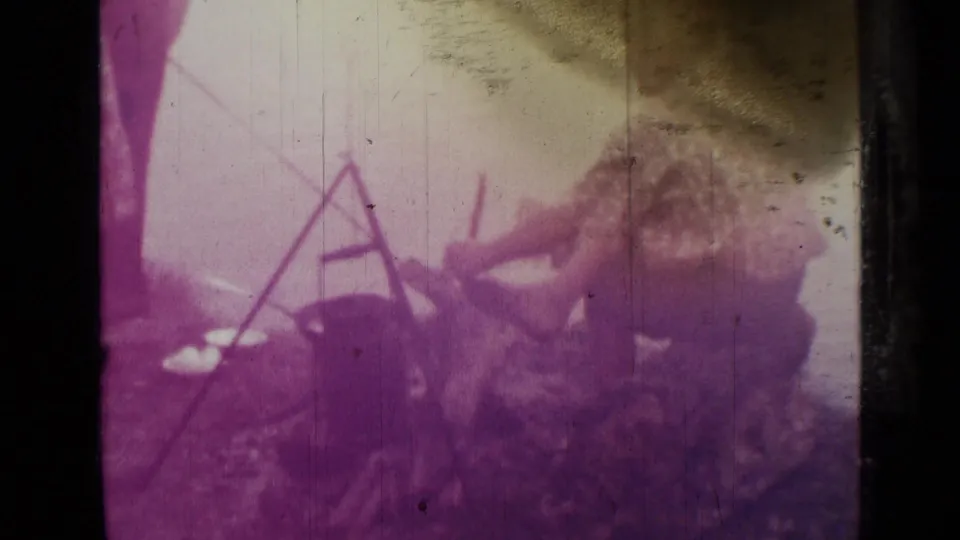 1967 Saint Petersburg home-movie frame with people gathered near a tripod cooking setup over open ground.