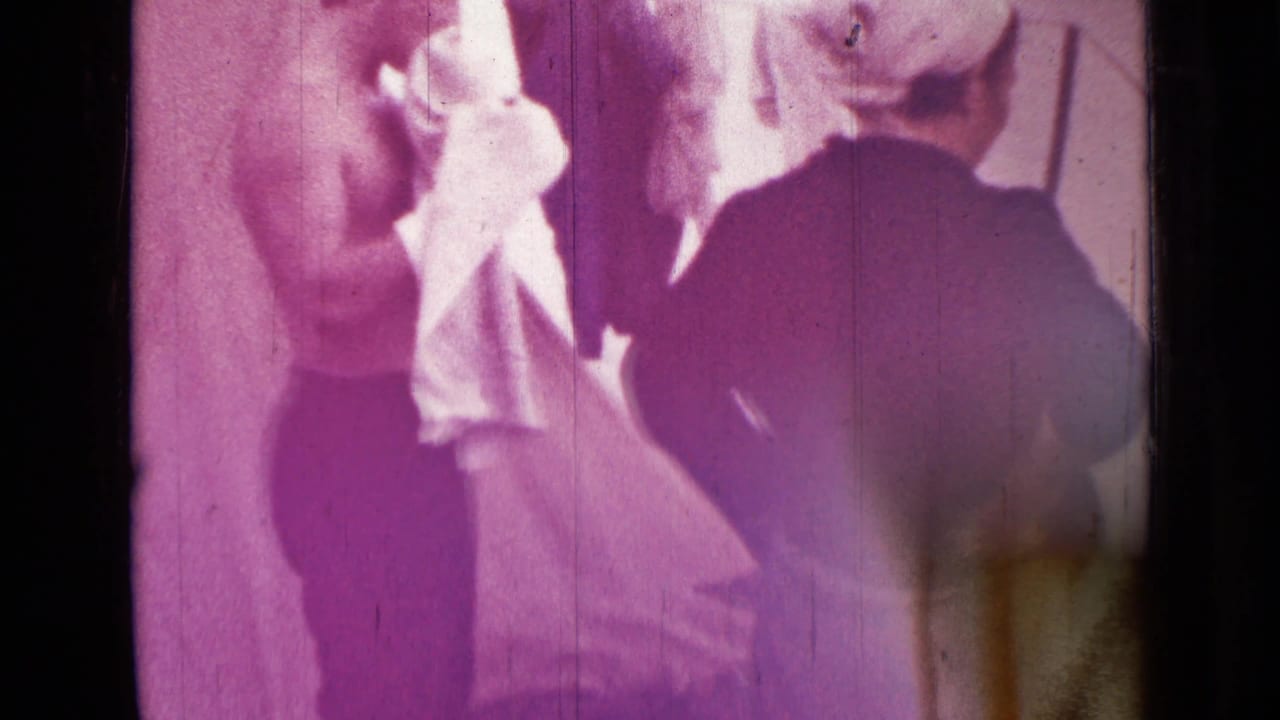 Shirtless man in dark trousers handles a white cloth near another partially visible person in 1967 Saint Petersburg home-movie footage.