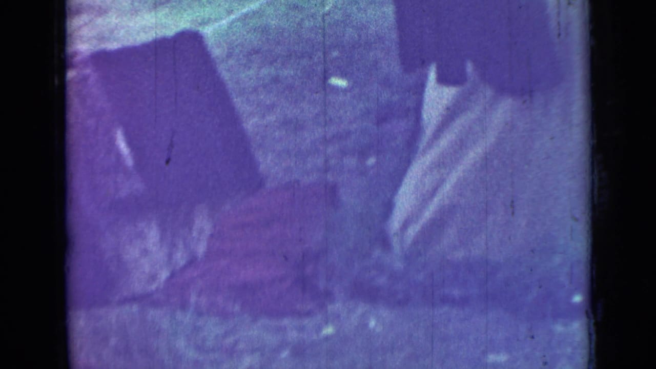 Dark purple-tinted close view of people near the ground, partly obscured by film exposure and borders.