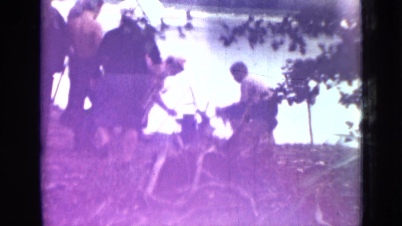 Several people beside a bright riverbank in Saint Petersburg, Russia, 1967, with one figure tending a small fire or wood pile.