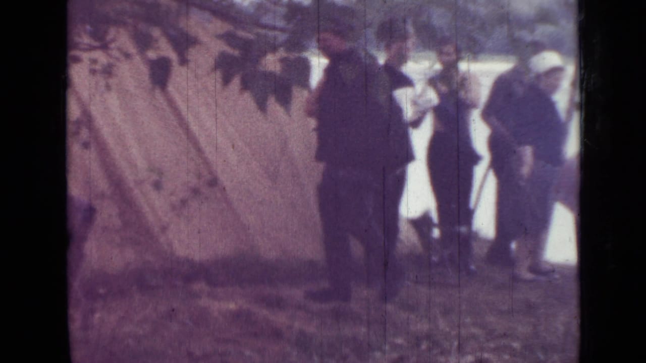 1967 home-movie footage near Saint Petersburg shows adults beside a pale tent, with lake water and trees visible beyond the campsite.