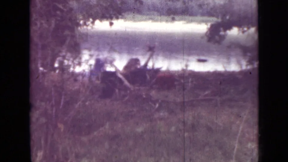 Purple-shifted 8mm frame showing wooded cover near water in Saint Petersburg, with an indistinct person faintly visible by the bank.