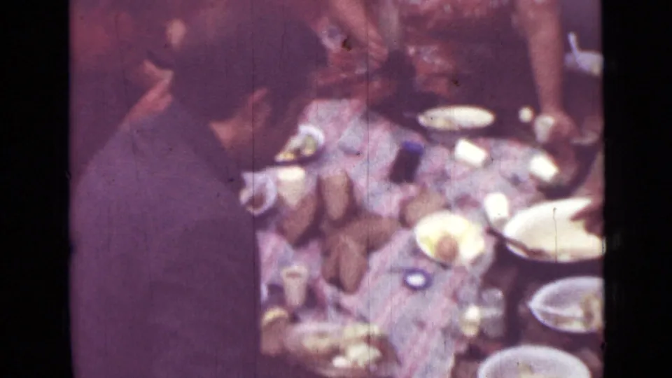 1967 Saint Petersburg 8mm frame showing a man beside a picnic blanket with plates, cups, food, and people partly visible around him.