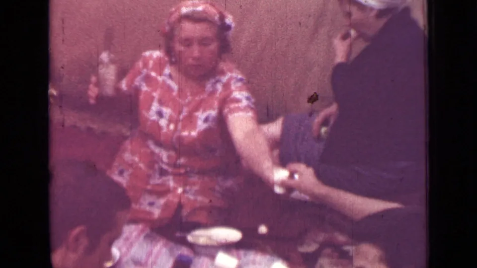 1967 Saint Petersburg home-movie frame of a woman in a patterned dress reaching across a private meal table toward another adult.