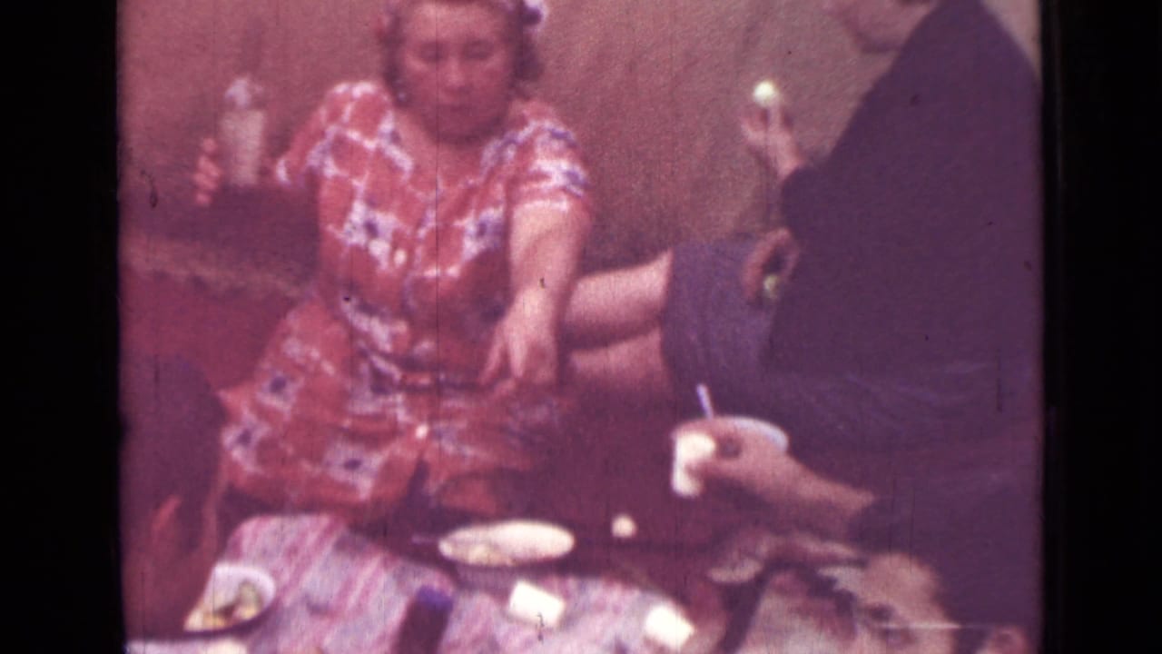Woman in a patterned dress seated at a picnic table with other adults partly visible.