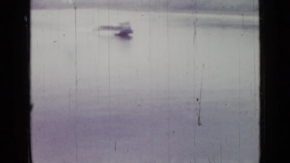 1967 8mm home-movie frame from Saint Petersburg metadata showing a small distant boat crossing calm lake water.