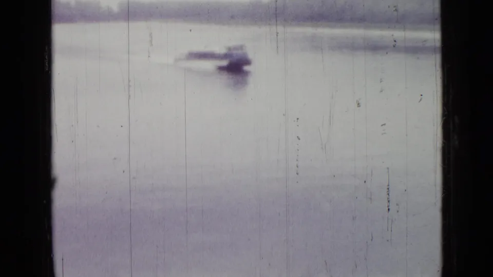 Distant small motorboat on pale water in 1967 Saint Petersburg home-movie footage, seen through soft focus and film wear.