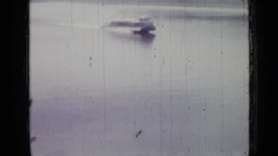 A small motorboat appears farther along the water, with a faint wake and visible 8mm scratches in the frame.