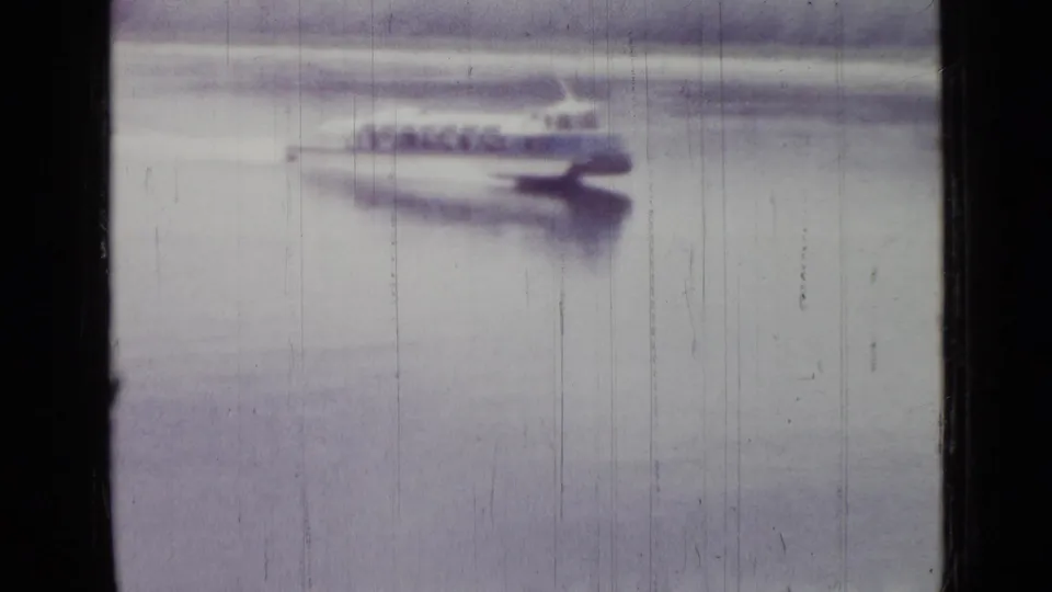 The motorboat reaches the right side of the frame, still blurred by distance and speed in worn 8mm footage.
