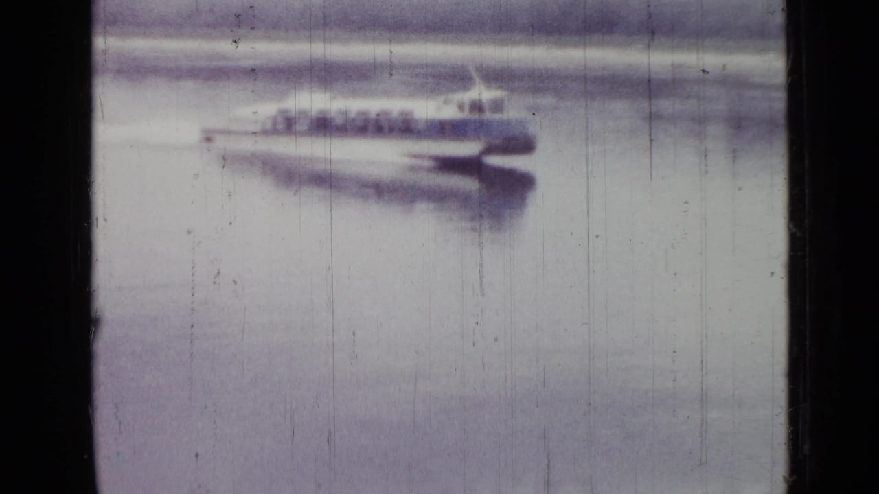 1967 Saint Petersburg home-movie frame of a streamlined white-and-blue boat moving across calm water, with a blurred reflection below.