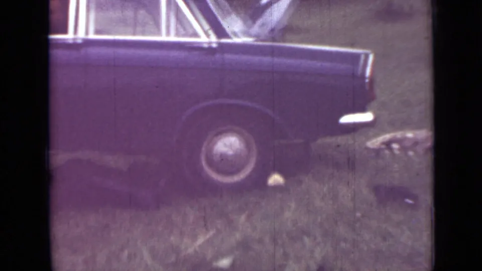 1967 Saint Petersburg home-movie frame showing the side of a dark sedan on grass, with the rear wheel and lower body in view.
