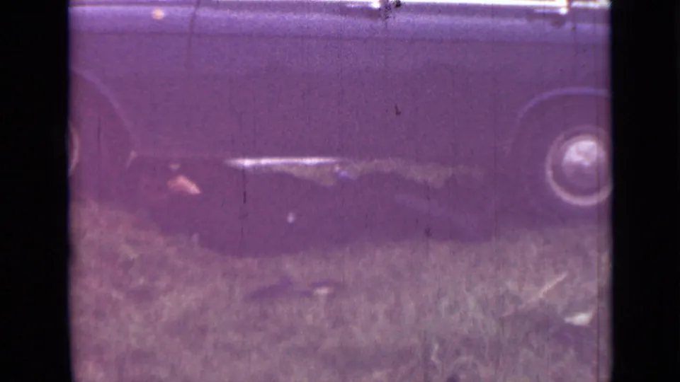 1967 Saint Petersburg 8mm frame of a dark car parked or stopped on grass, with one wheel visible and strong magenta-purple aging in the scan.