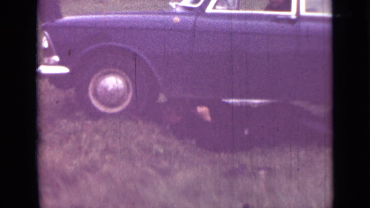 Dark sedan on grass with a person partly visible beneath the side.