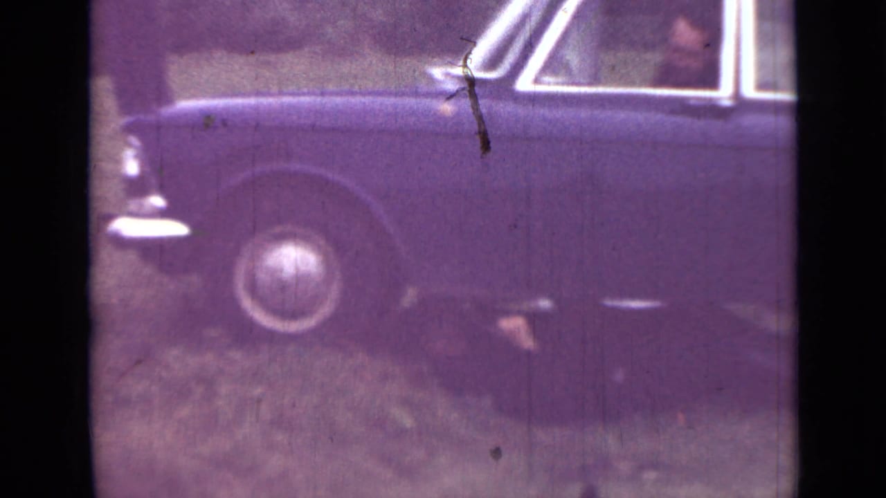 Side of a dark sedan with wheel, windows and a person partly under the car.