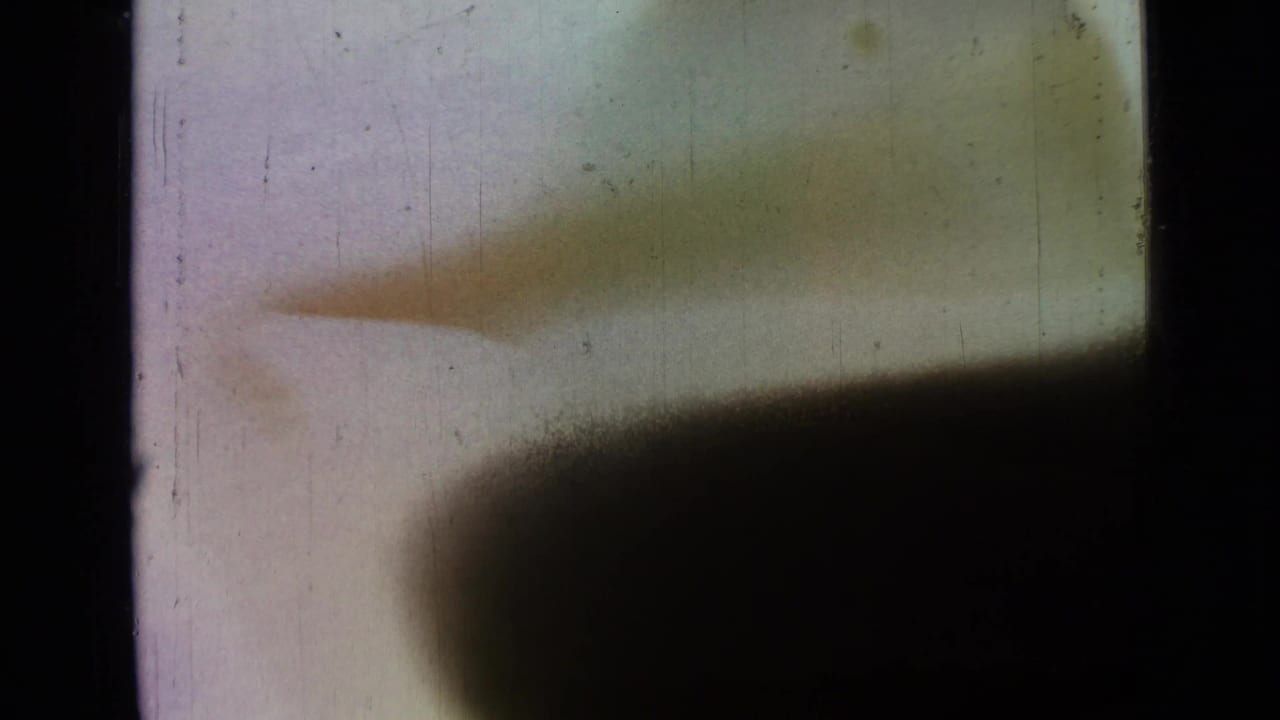 1967 8mm lakeside frame showing a sloped natural bank under soft light, partly obscured by heavy shadow and film wear.