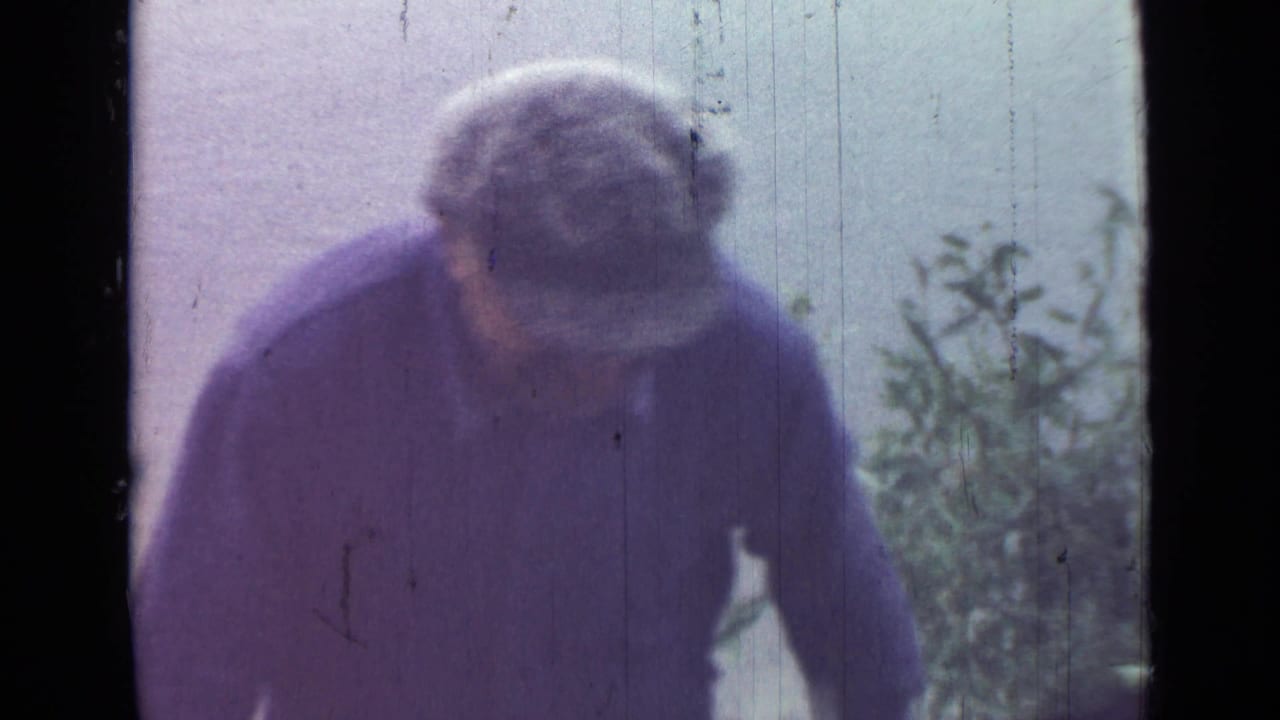 In 1967 Saint Petersburg home-movie footage, an adult man in a patterned cap and dark jacket leans toward the camera outdoors.