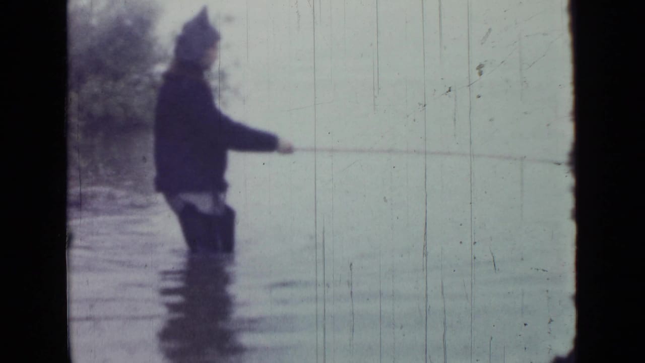 Wide 1967 Saint Petersburg frame shows an adult man wading in shallow lake water while extending a fishing line from shore.