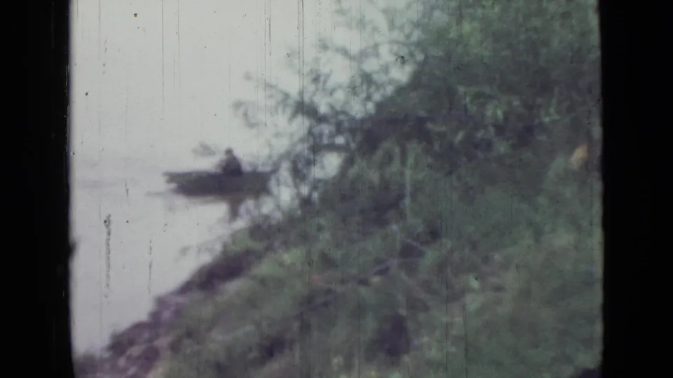 1967 Saint Petersburg 8mm frame showing the rower lower in frame near a leafy shoreline and reflected water.