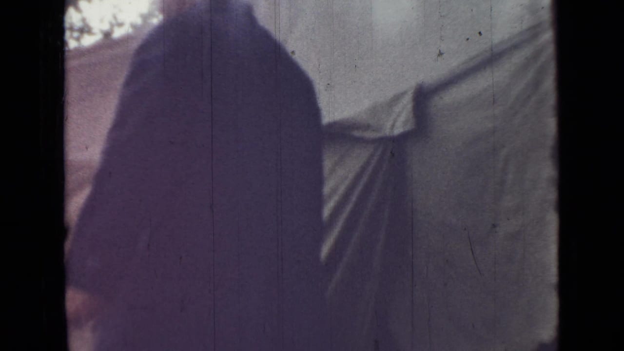 1967 Saint Petersburg home-movie frame shifts from the rower to close hanging fabric or sheets beside an indistinct outdoor structure.