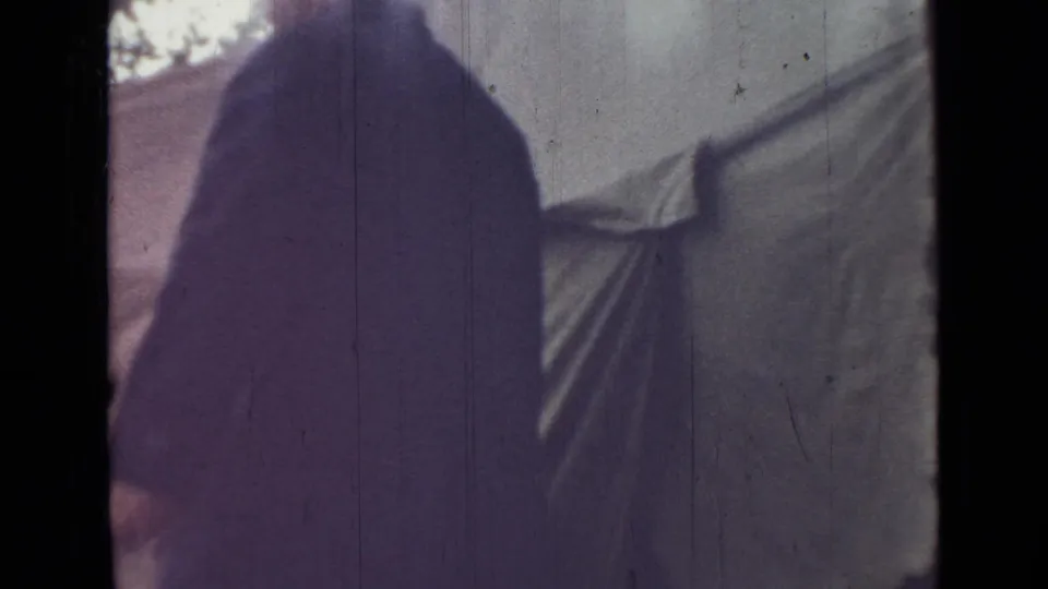 1967 Saint Petersburg home-movie frame shifts from the rower to close hanging fabric or sheets beside an indistinct outdoor structure.