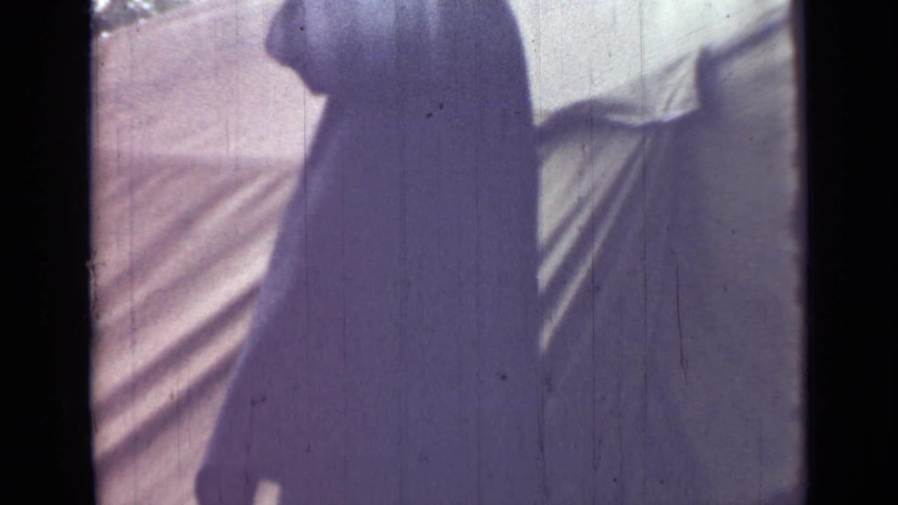 The man appears in profile near canvas tenting, his face partly obscured by shadow and soft 8mm focus.