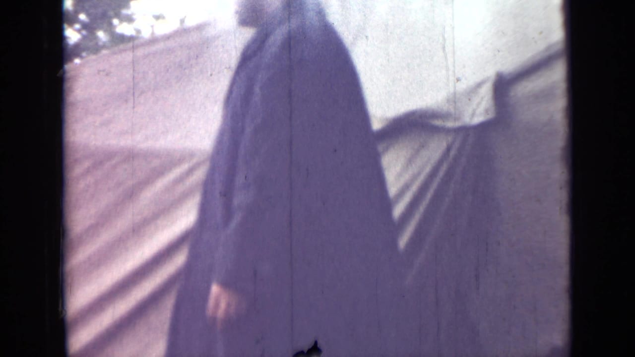 The man in a long dark coat walks past pale canvas tenting in the stated 1967 Saint Petersburg home-movie clip.