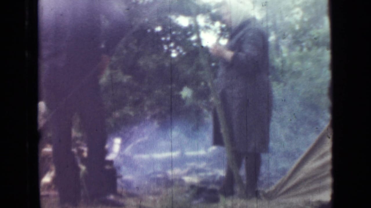 1967 camping footage near Saint Petersburg with adults standing beside smoke from a small campfire, framed by trees and a tent edge.