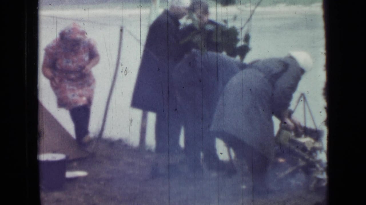 1967 Saint Petersburg riverside campsite frame showing adults beside a canvas tent, with one person bending over equipment or vegetation.