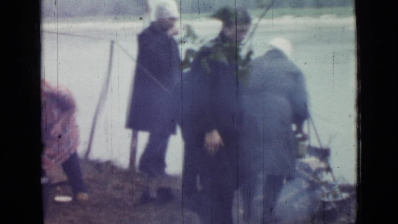Two adults are prominent beside a lakeside tent in 1967 Russia home-movie footage, with camp gear and water behind them.